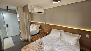 Hotellihuone, jossa on suuri sänky, yöpöytä, vaatekaappi ja ilmastointilaite.