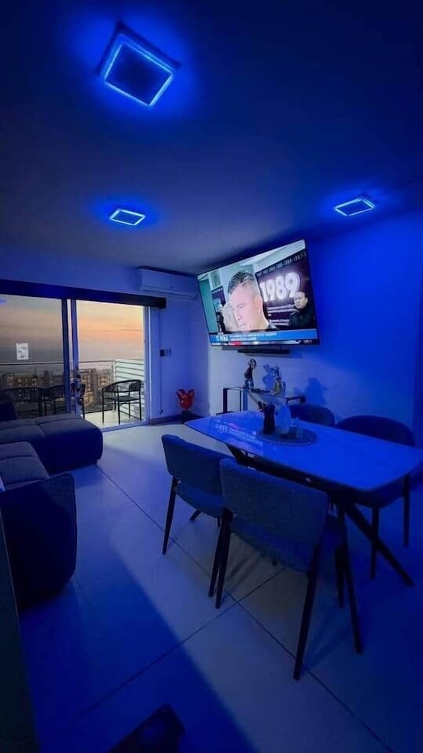 A modern living room with a flat-screen TV, a dining table, and a sofa.