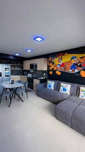 A modern kitchen with a dining area, a gray sofa with cartoon-themed pillows, and a mural on the wall.