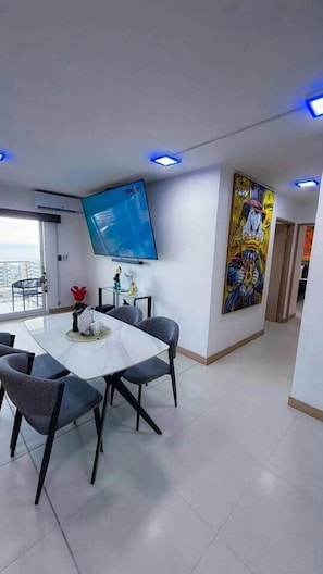 A modern hotel room with a dining area, a flat-screen TV, and a large artwork on the wall.