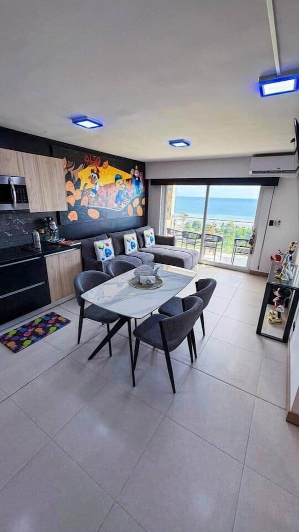 A modern kitchen with a dining area, a large window with a view of the ocean, and a colorful mural on the wall.
