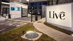 Een goed verlicht buitengebied met een 'Live'-bord, moderne architectuur en een grasveldentree.