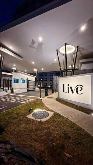 A well-lit outdoor area with a 'Live' sign, modern architecture, and a grassy entrance.