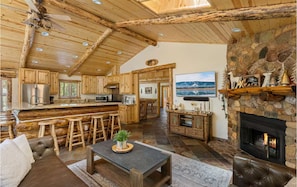 A log cabin interior with a stone fireplace, wooden bar, and a large window overlooking the landscape. - Family Cabin, 2 Game Rooms, Basketball Court, Spa (Big Bear Lake,)