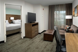 A hotel room with a bed, a television on a wooden stand, a desk with a chair, and a window with curtains.