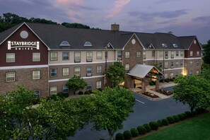 Een Staybridge Suites hotel met een gevel van baksteen, meerdere ramen en een verzorgd gazon.