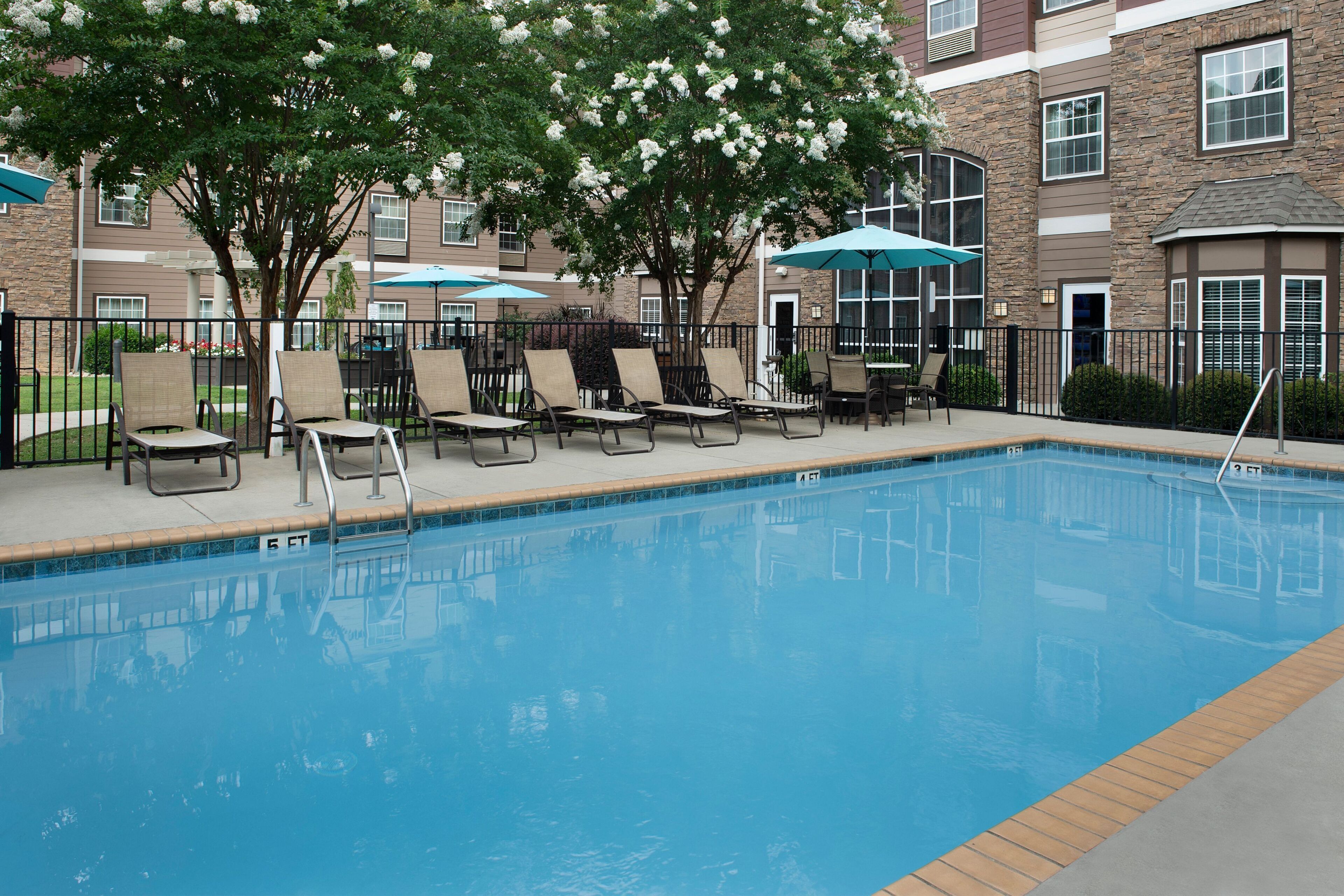 A swimming pool with lounge chairs and umbrellas, surrounded by a brick building with windows.