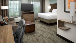 A hotel room with a bed, a TV, a desk, a chair, a lamp, and a window with curtains.