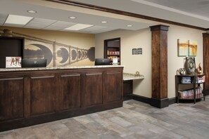 A reception area with a marble counter, wooden cabinets, a laptop, a bookshelf, and a wall mural. - 1BR King Suite w/ Kitchen | Pool + Hot Breakfast (Greenville)