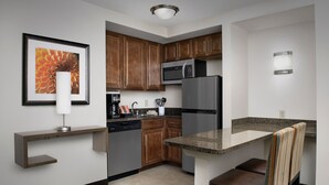 A modern kitchen with wooden cabinets, a stainless steel refrigerator, a microwave, and a dining area with a striped chair.
