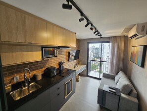 Eine moderne Küche mit schwarzem Arbeitsplatz, Spüle aus Edelstahl und einem eingebauten Ofen. Es gibt einen Essbereich mit einer grauen Couch und einem an der Wand befestigten Fernseher.