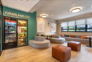 Ein modernes Interieur mit einem 'Grab and Go' Kühlschrank, Sitzbereichen und großen Fenstern.