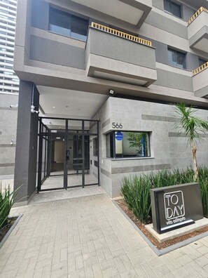 A modern building with a glass entrance, a number '566' sign, and a sign that says 'TO DAY.' - Apartamento Confortável – Vila Olímpia (São Paulo)