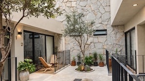 Un patio moderno al aire libre con paredes de piedra, una zona de estar con sillas y plantas en macetas.