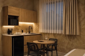 A compact kitchen with a coffee machine, a microwave, and a sink. There is a dining area with two chairs and a table.