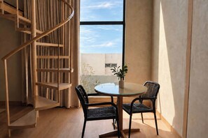 A modern interior with a spiral staircase, a round glass table, two wicker chairs, and a view of the sky through a large window. - SWEVEN Hotel Boutique (Guadalajara)