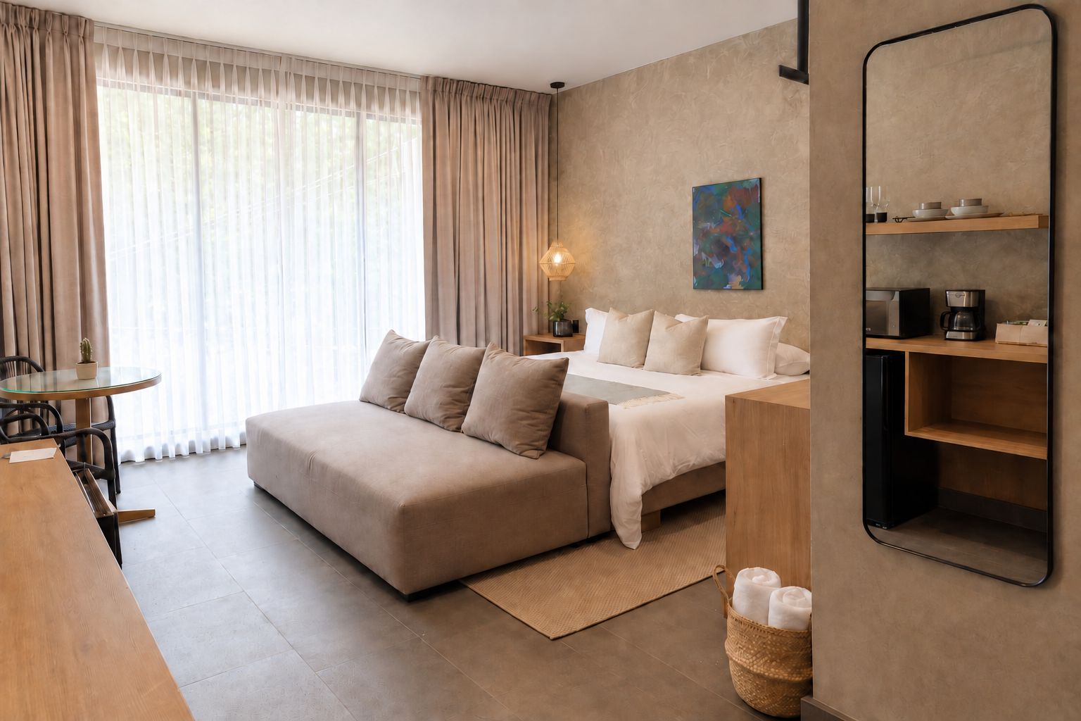 A hotel room with a bed, a sofa, a dining table, and a small kitchen area.
