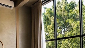 A modern living room with a sofa, a small table with a plant, and a view of trees through large windows. - SWEVEN Hotel Boutique (Guadalajara)