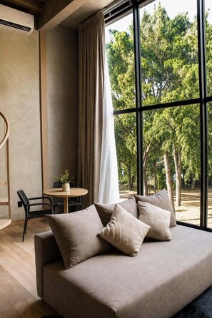 Un salon moderne avec un canapé, une petite table sur laquelle est posée une plante, et une vue sur les arbres à travers de grandes fenêtres.