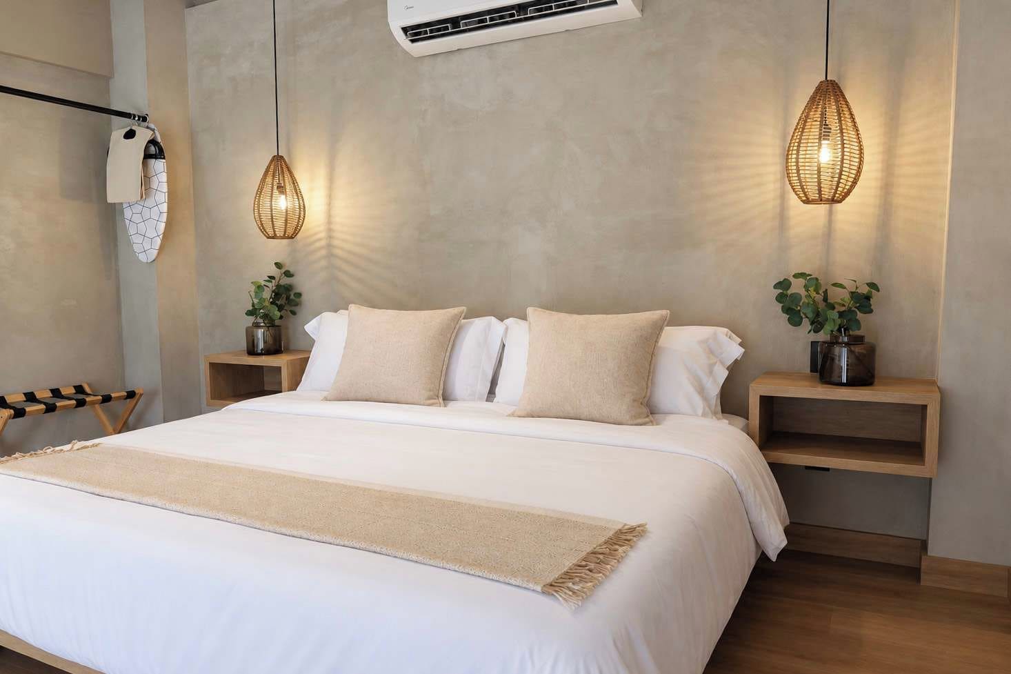Un dormitorio con una cama grande, dos mesitas de noche con plantas, una lámpara colgante y un aire acondicionado de pared.