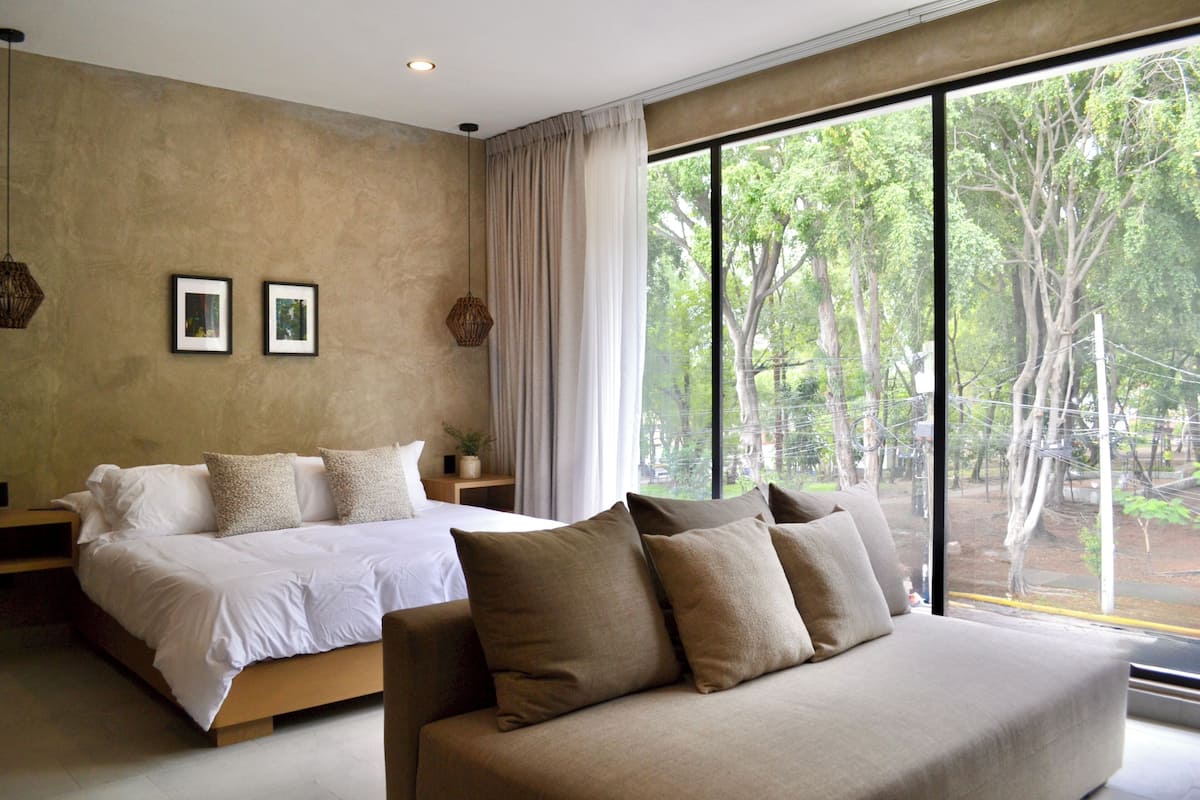 Quarto com uma cama grande, um sofá e vista para árvores pela janela.