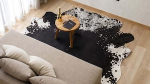 A living room with a sofa, a round wooden table with a bottle and glasses, a black and white cowhide rug, and a mounted flat-screen TV. - SWEVEN Hotel Boutique (Guadalajara)