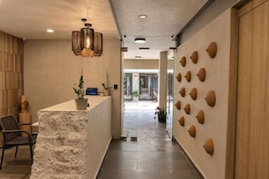 Un área de recepción con mostrador de mármol, pared de madera con detalles decorativos y una lámpara colgante moderna.