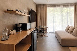 Una habitación de hotel moderna con un escritorio de madera, un televisor de pantalla plana, un sofá y una zona de comedor con mesa y sillas.