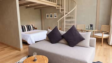 A modern bedroom with a bed, a sofa, a small table, and a staircase.