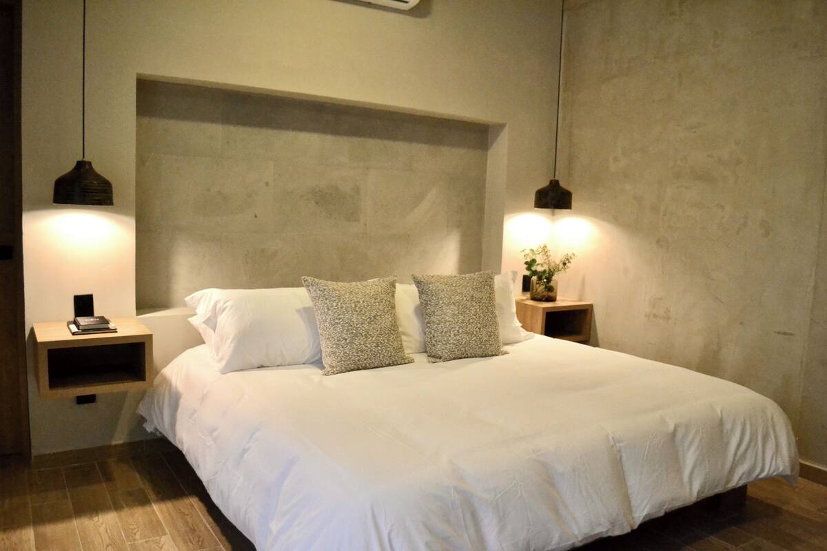 Quarto com cama grande, duas mesas de cabeceira e duas luminárias pendentes.