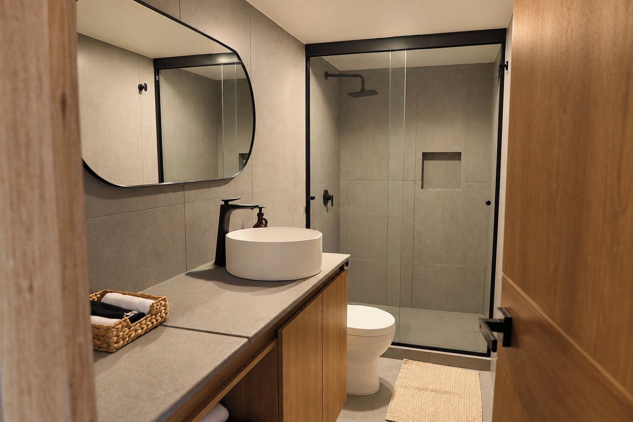 Un baño moderno con un lavabo redondo, inodoro y ducha con mampara de vidrio.