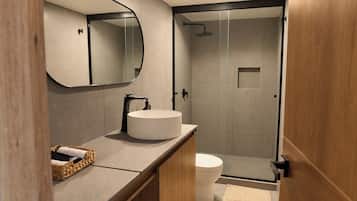 Un baño moderno con un lavabo redondo, inodoro y ducha con mampara de vidrio.