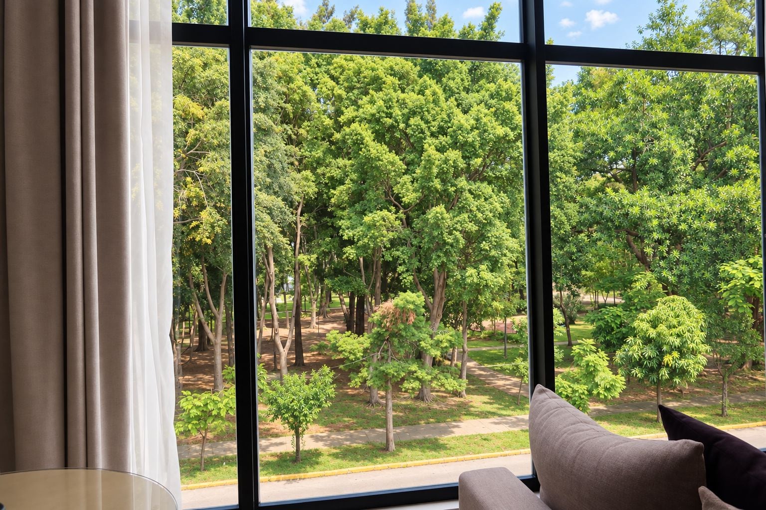 A room with a large window offering a view of a green park with trees and a pathway.