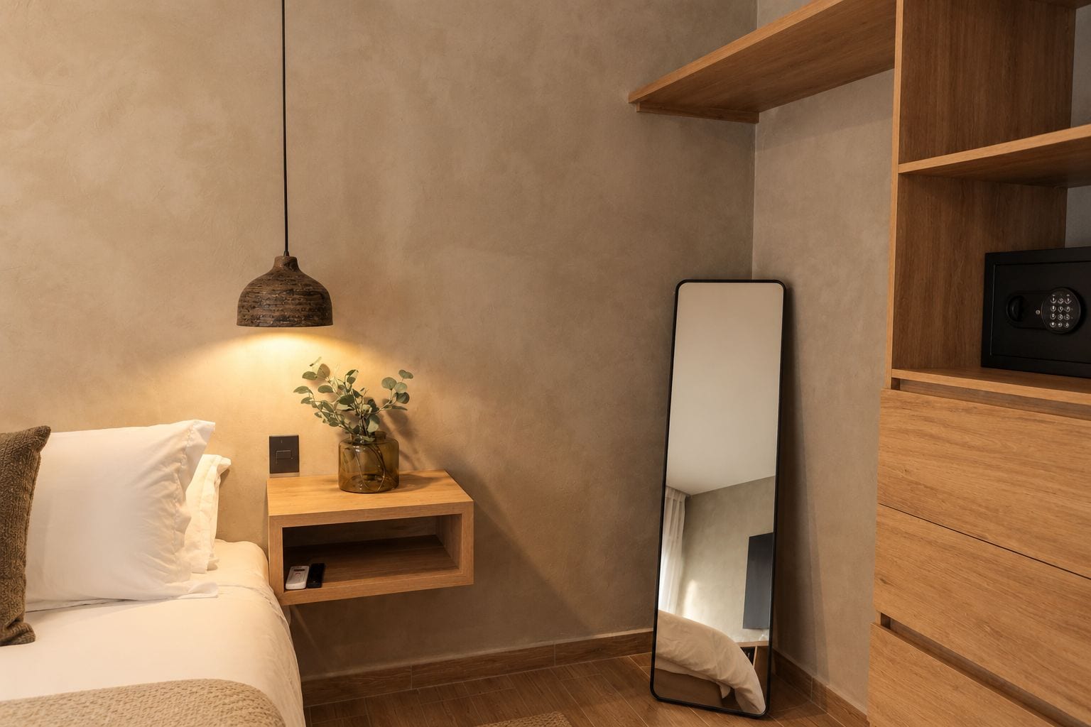 A bedroom with a bed, bedside table, nightstand, mirror, and a hanging light fixture.