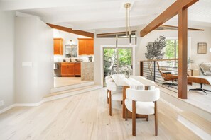 Ein moderner Essbereich mit einem langen Tisch und Stühlen, im Hintergrund eine Küche und eine Treppe, die zu einer weiteren Ebene führt.
