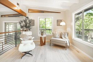 Ein modernes Wohnzimmer mit einem weißen Sofa, einem runden Couchtisch und einem Beistelltisch mit Lampe. Durch die Fenster ist ein Balkon zu sehen.
