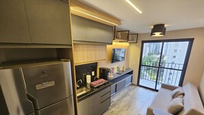 Una cucina moderna con frigorifero, fornelli e lavello, un'area pranzo con divano, e un balcone con vista.