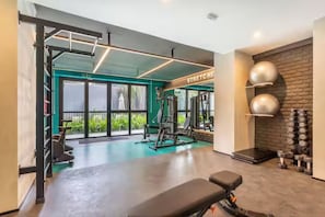 Ein Fitnessraum mit Trainingsgeräten, einer Bank und einer Wand voller Kurzhanteln.