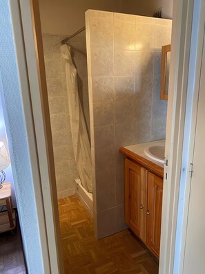 A bathroom with a shower, a wooden cabinet, and a tiled wall.