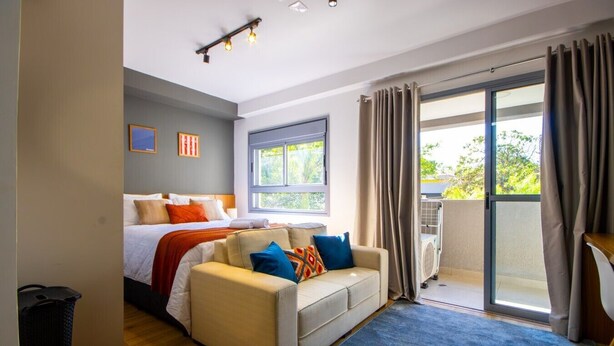 Una habitación de hotel moderna con una cama, un sofá, un ventanal grande y un cerramiento de vidrio corredizo que da a un espacio al aire libre.