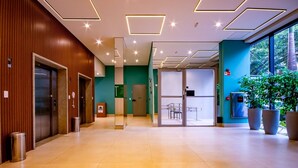 Un moderno vestíbulo con pared de madera, mostrador de recepción, puerta de entrada de vidrio y plantas en macetas.