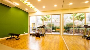Un gimnasio con equipo de ejercicio, ventanas amplias y una pared verde.