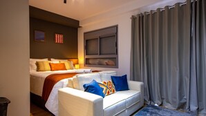 Habitación de hotel con cama, sofá, ventana con persianas y cortina.