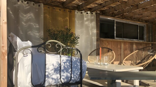 Een overdekt terras met een tafel, stoelen en een metalen bedframe.