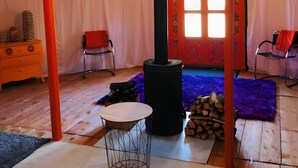 Een tent met een schoorsteen in het midden, een ronde tafel, stoelen, een dressoir en een raam met gordijnen.
