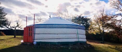 A yurt with a red door, white and blue patterned walls, and a snow-covered roof.