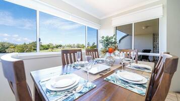 A dining area with a table set for four, large windows, and a view of greenery outside.