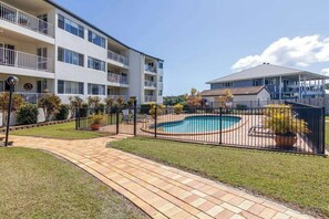A residential building with a swimming pool, a fenced patio, and a well-maintained lawn. - 3BR Apt + Pool Great Location Opp Beach & Park (Urangan)