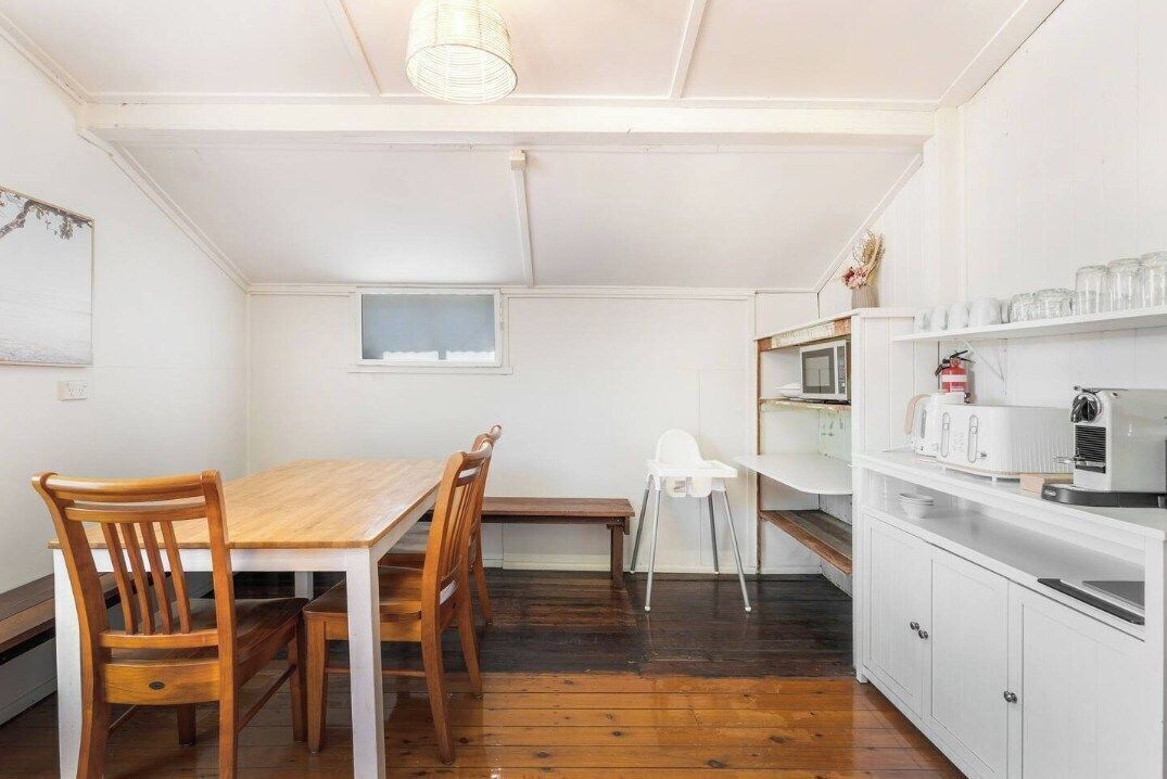 A compact kitchen with a wooden table and chairs, a white cabinet with appliances, and a small window.