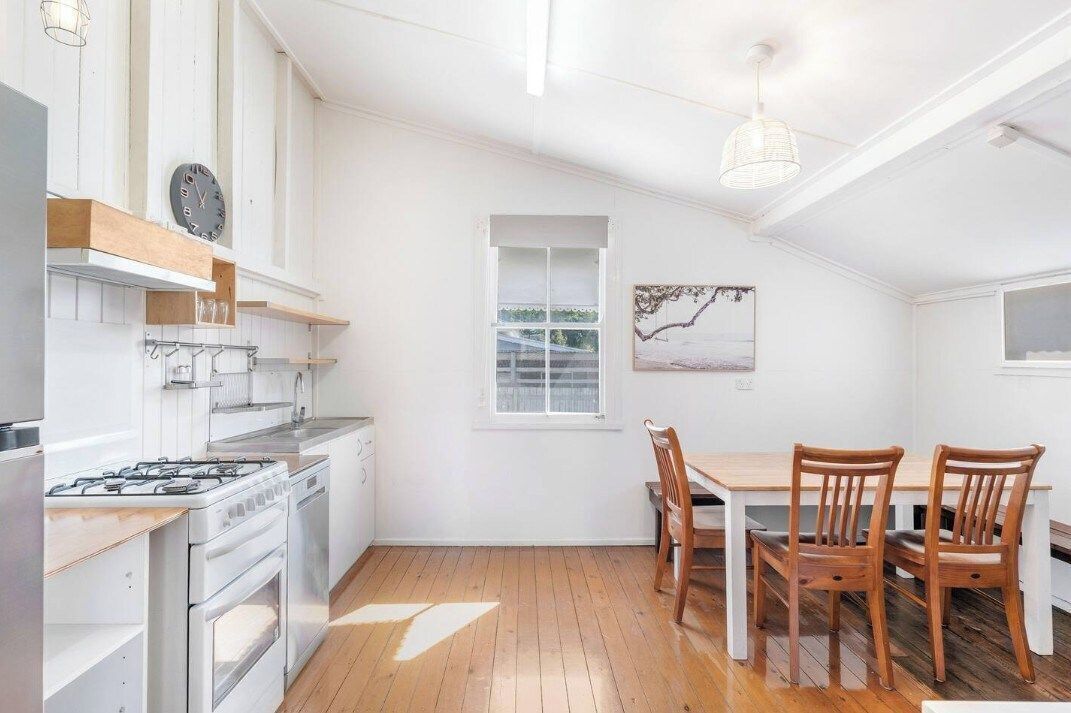 Una cocina con armarios blancos, una estufa y una zona de comedor con sillas de madera y una mesa.
